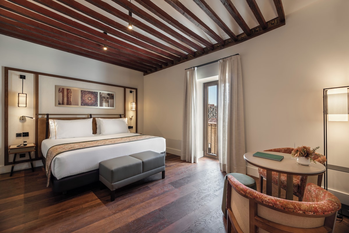Un dormitorio con una cama grande, una mesita de noche con un florero y una silla.
