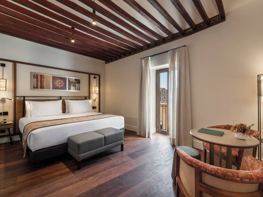 Un dormitorio con una cama grande, una mesita de noche con un florero y una silla.
