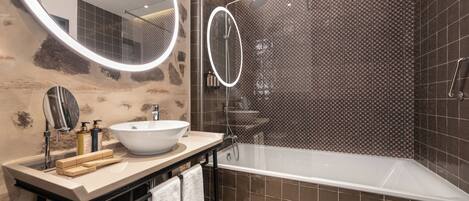 A modern bathroom with a large oval mirror, a round mirror, a white sink, and a freestanding bathtub.