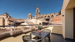 A balcony with a table and chairs, a potted plant, and a view of historic buildings with a prominent tower. - Áurea Toledo (Toledo)