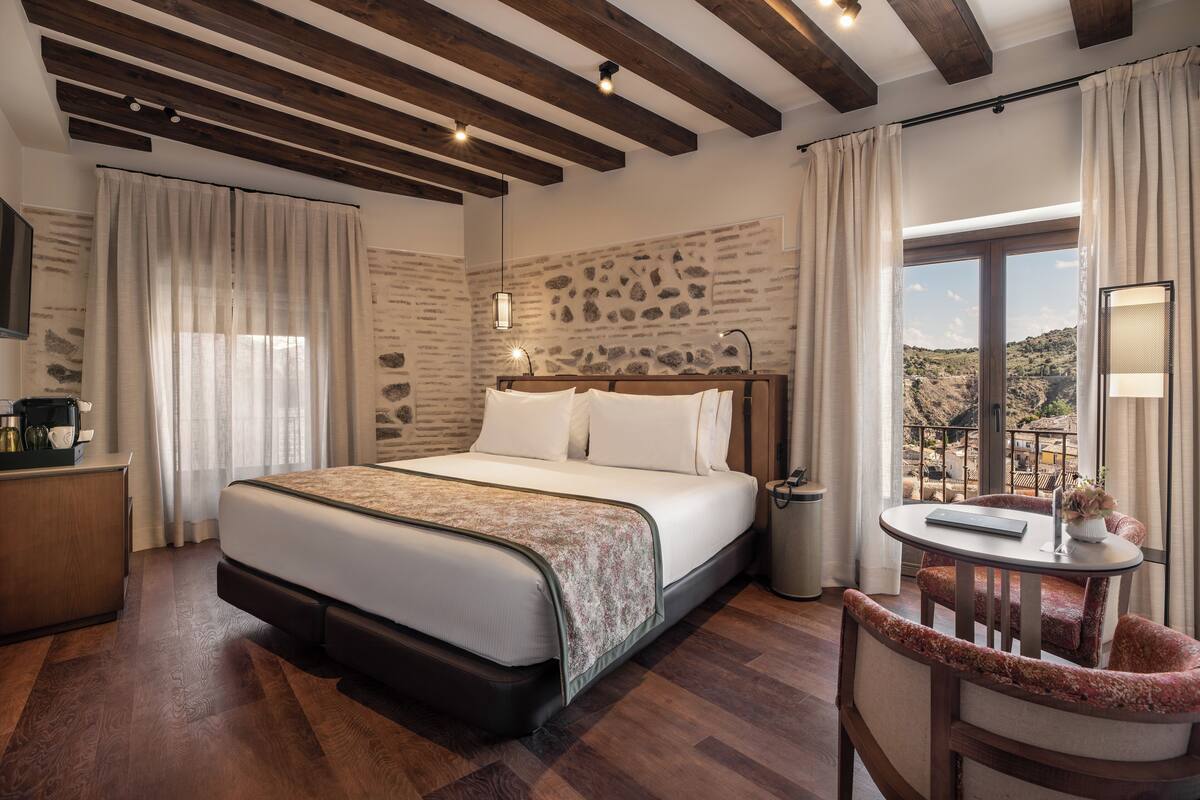 Habitación de hotel con cama, escritorio, silla, una mesita y vistas al exterior.
