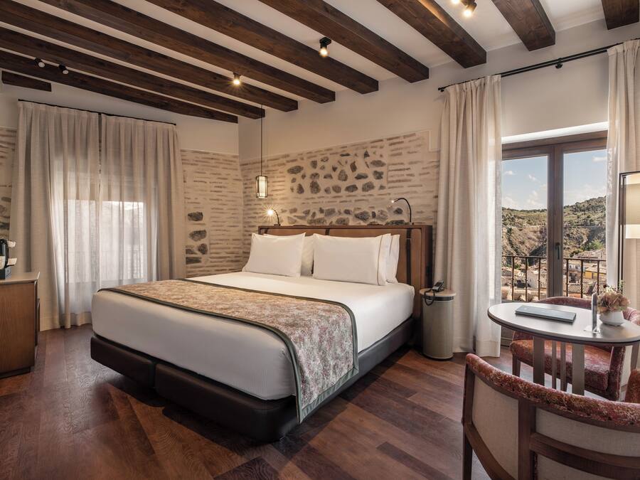 Habitación de hotel con cama, escritorio, silla, una mesita y vistas al exterior.
