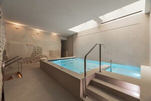 Un moderno espacio de spa con una amplia piscina rectangular, una escalera que conduce a un nivel superior y un tragaluz arriba.