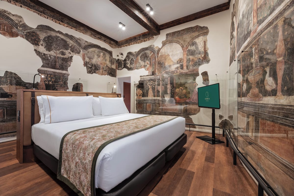 Una habitaci ón de hotel con una cama grande, suelo de madera y un mural de arquitectura clásica en las paredes.
