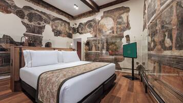 A hotel room with a large bed, wooden flooring, and a mural of classical architecture on the walls.