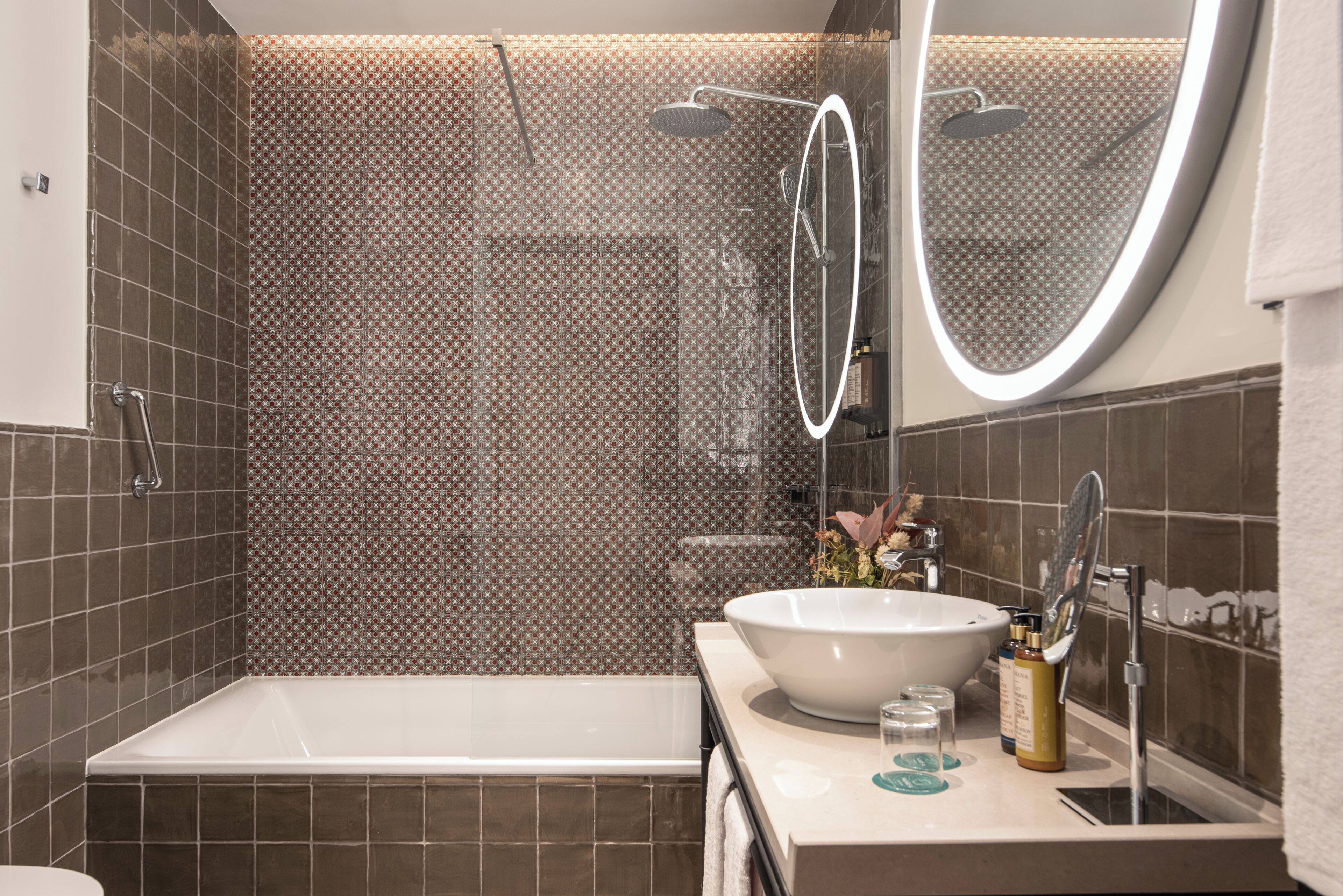 A modern bathroom with a large bathtub, a round mirror, and a sink with toiletries.