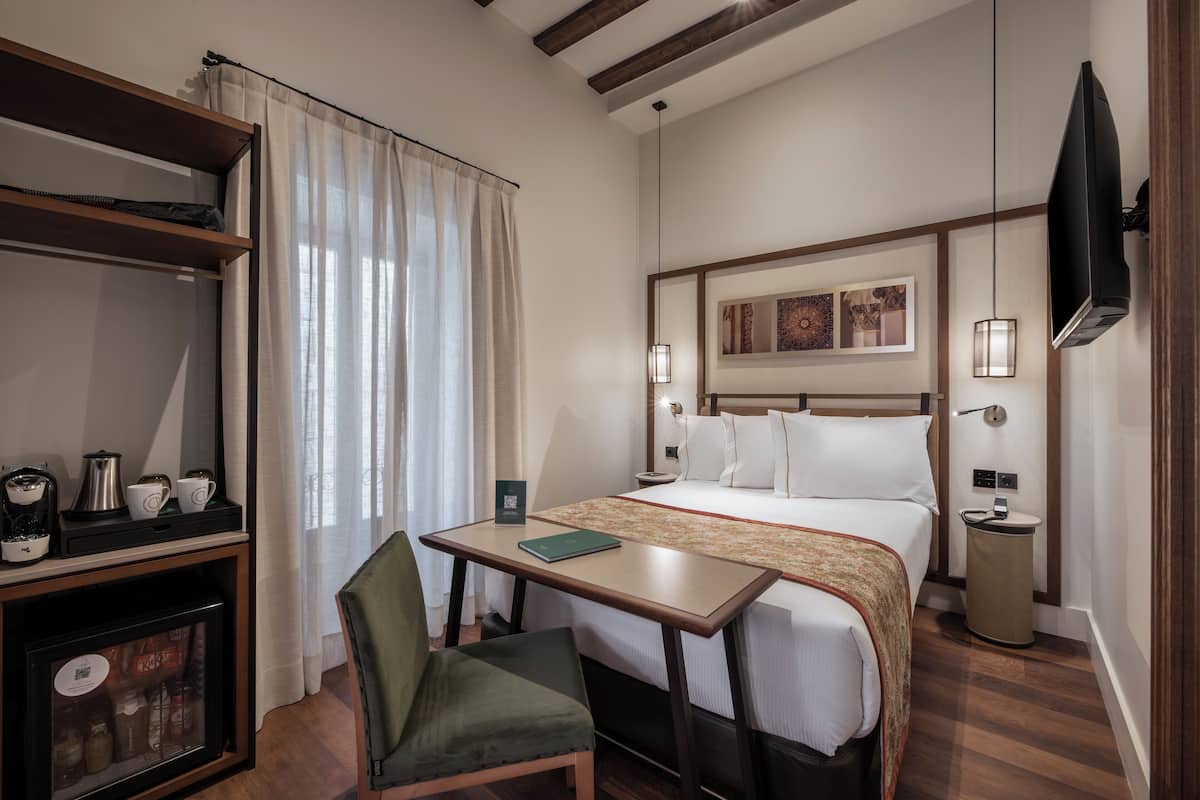 Una habitación de hotel con cama, escritorio, silla, televisor y estante con equipo para preparar café.