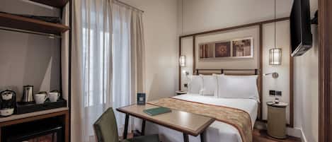 A hotel room with a bed, a desk, a chair, a TV, and a shelf with coffee-making equipment.