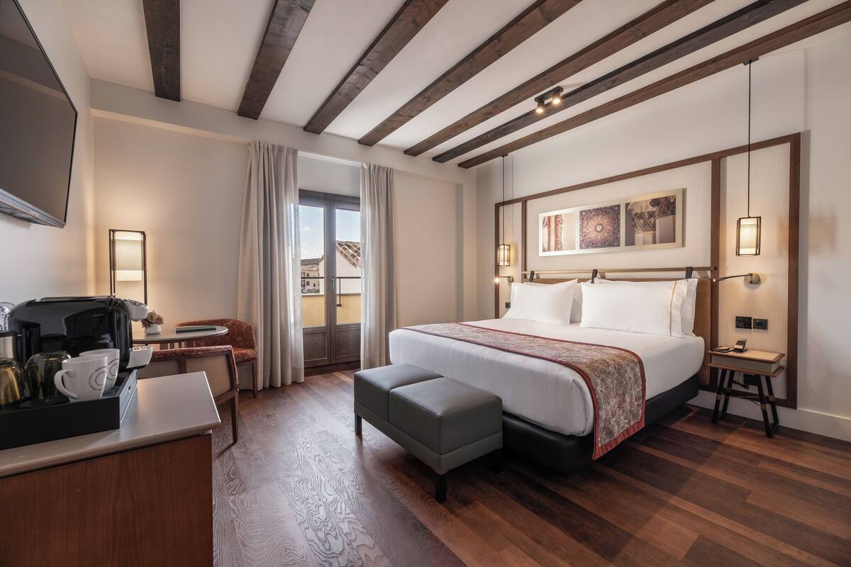 Habitación de hotel con una cama grande, un escritorio con cafetera, una silla y vistas al exterior.
