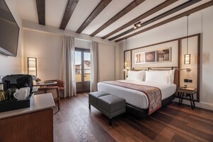 Habitación de hotel con una cama grande, un escritorio con cafetera, una silla y vistas al exterior.