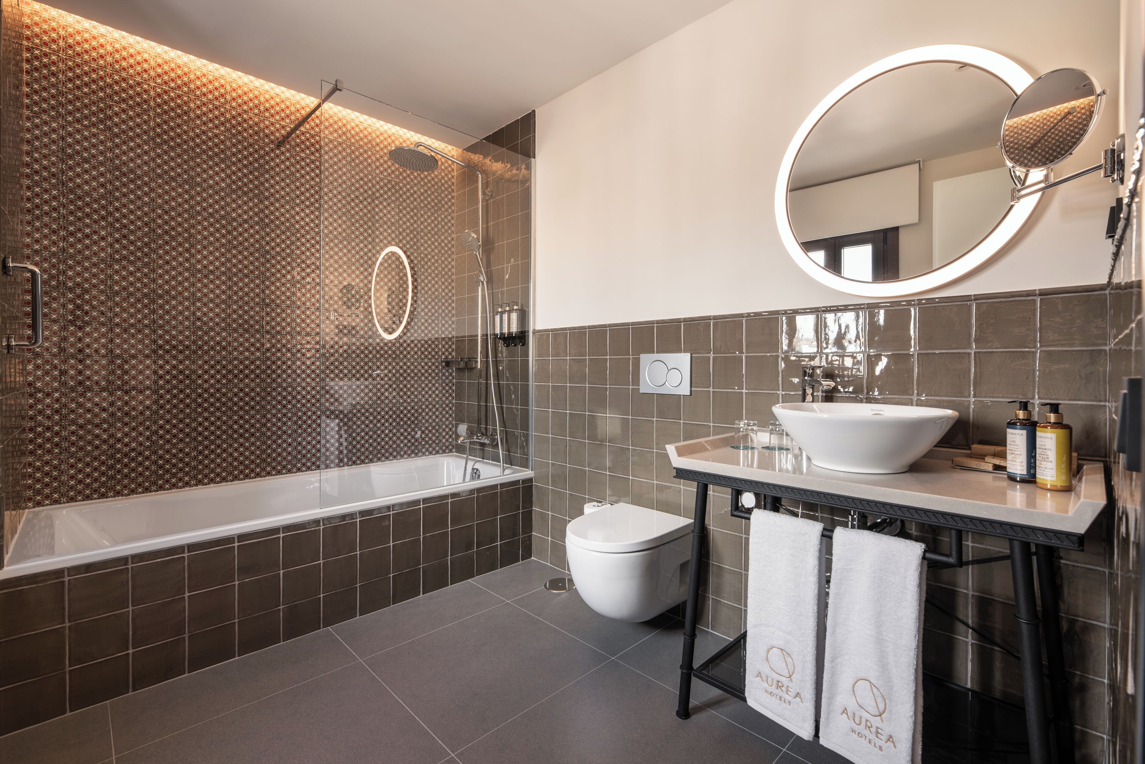 Un baño moderno con una bañera, un lavamanos y un inodoro. Hay toallas colgadas en la pared y un espejo sobre el lavamanos.