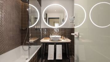 A modern bathroom with a bathtub, a sink, and a shower. There are two towels hanging on a rack.