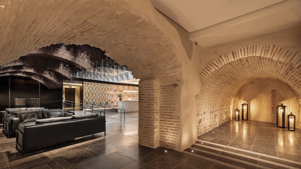 A modern lobby with a black leather sofa, a patterned wall, and a stone archway. - Áurea Toledo (Toledo)