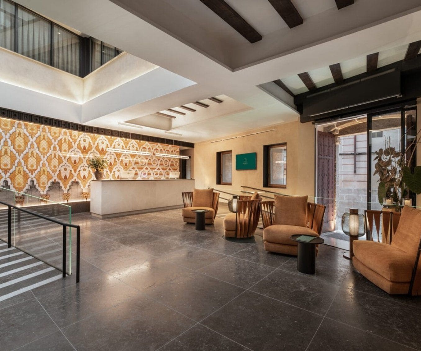 A spacious lobby with a high ceiling, a patterned wall, and a seating area with sofas and chairs.