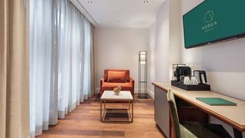 Une chambre d’hôtel équipée d’un canapé, d’une table basse, d’un bureau avec une chaise, d’un téléviseur à écran plat et d’une lampe.