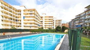 A swimming pool with a wooden deck, surrounded by multi-story residential buildings with balconies. - ADRIAN Apartment (La Pineda)