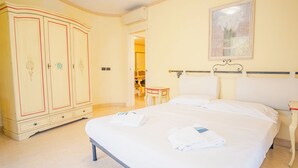 Una habitación de hotel con una cama grande, un armario, una mesita pequeña y un cuadro en la pared.