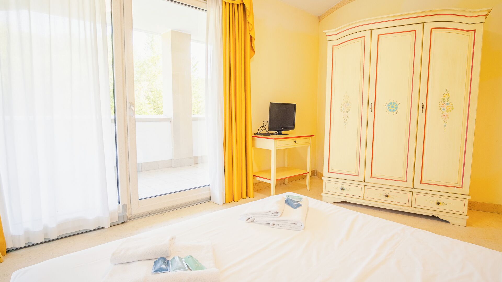 Une chambre d’hôtel comprenant un lit, un bureau avec un ordinateur, une armoire et une porte-fenêtre coulissante.