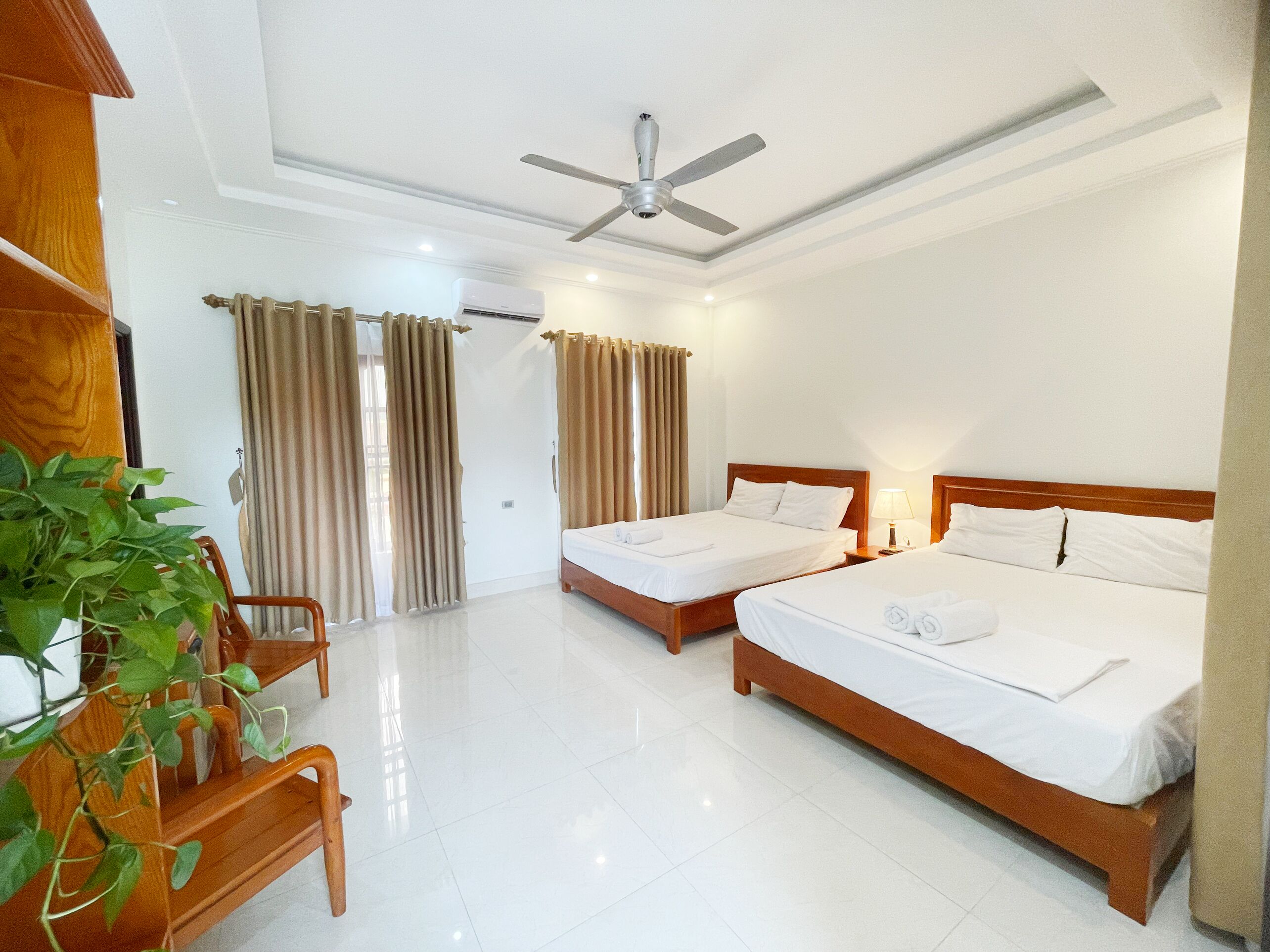 A hotel room with two beds, a ceiling fan, and a potted plant.