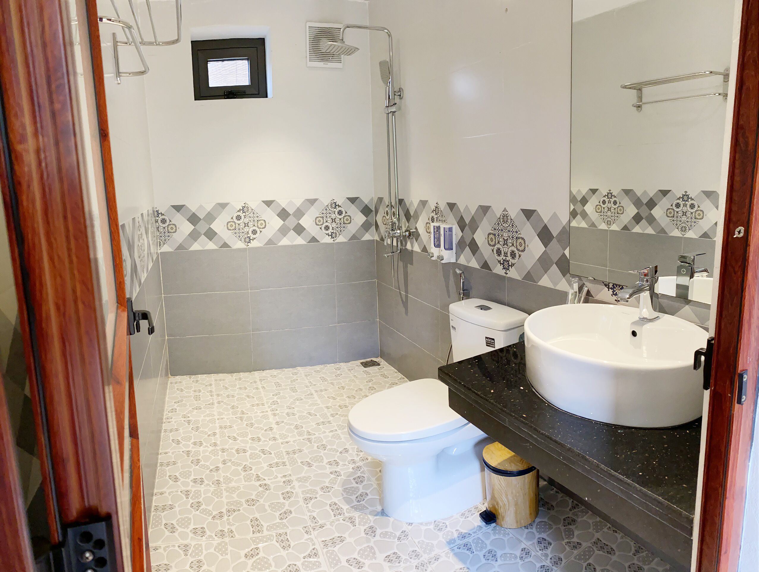 Un baño con inodoro, bidé y lavamanos, con azulejos estampados y suelo de madera.