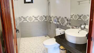 Un baño con inodoro, bidé y lavamanos, con azulejos estampados y suelo de madera.