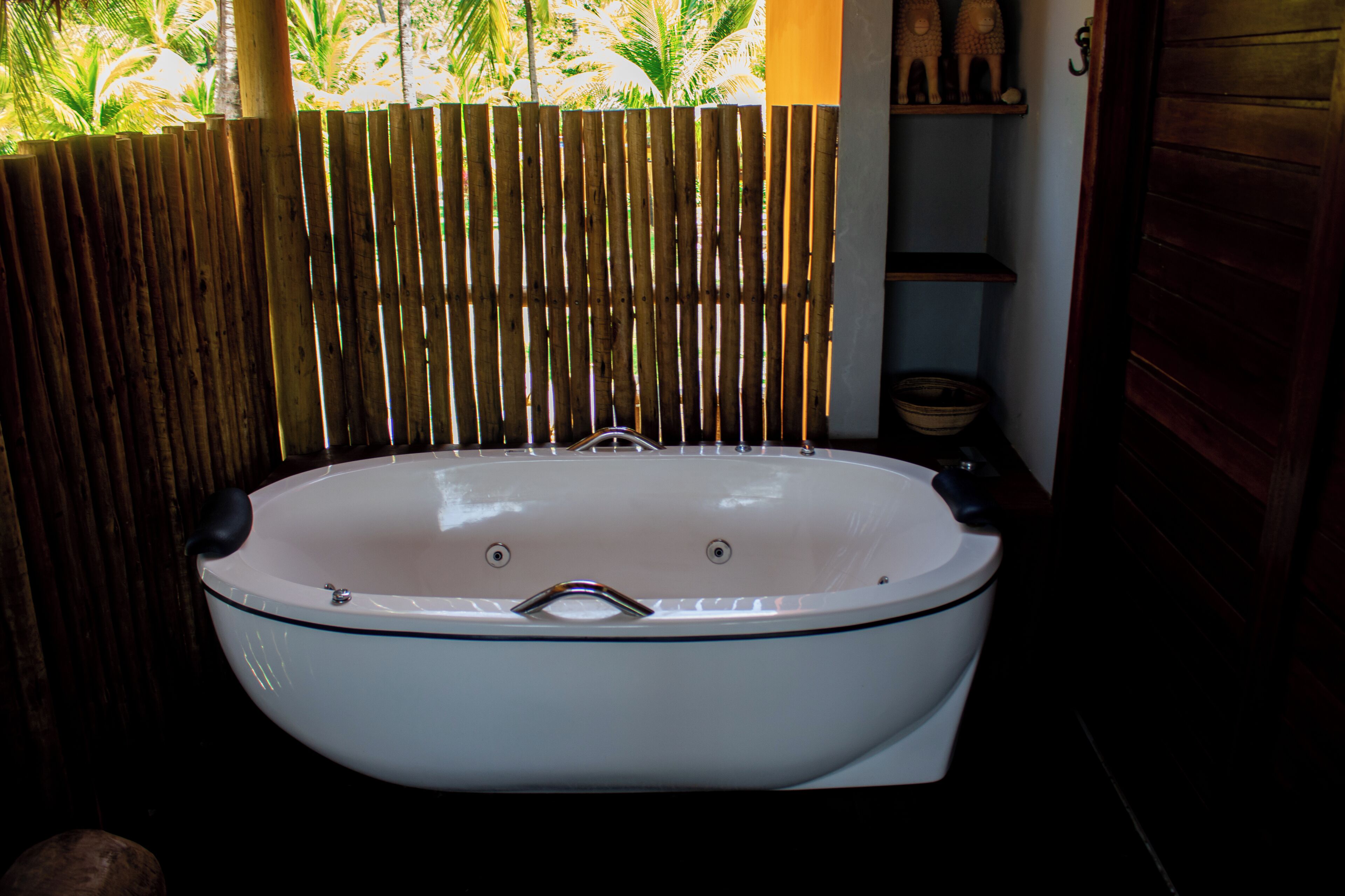 A white freestanding bathtub in a bathroom with a bamboo fence and a shelf with decorative items.