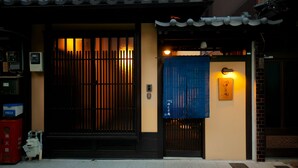 A traditional Japanese building with a black gate, a blue awning, and a sign with Japanese characters. - Tikkan Tsuyukusa-An (Kyoto)