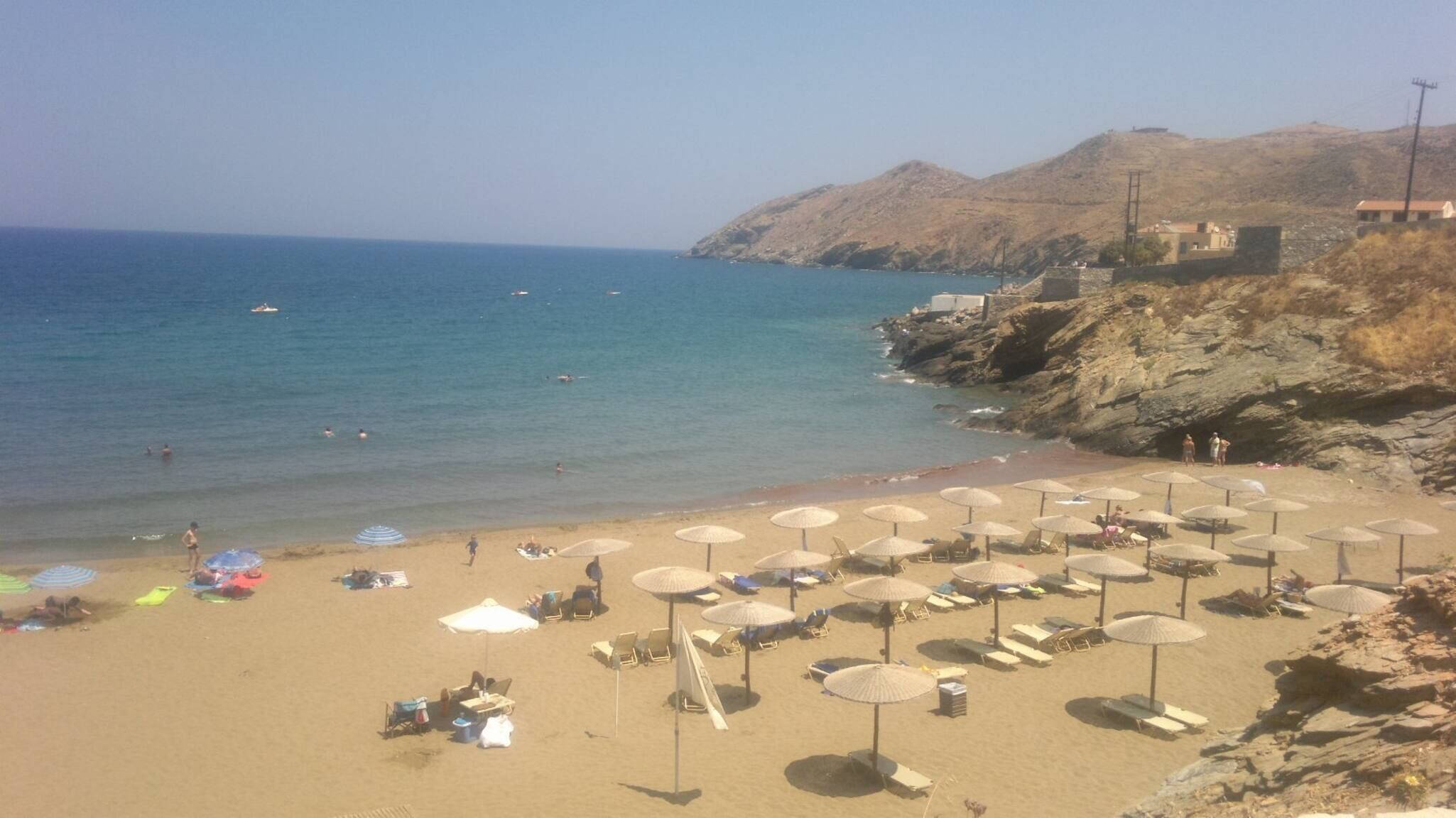 Een strand met ligbedden en parasols, een rotsachtige kustlijn en een heldere lucht.