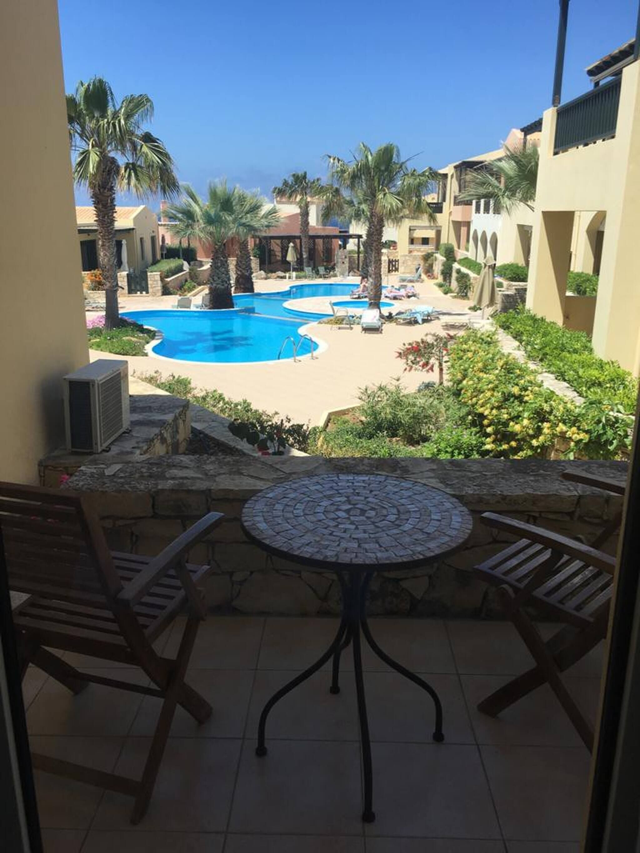 Ein Balkon mit Blick auf einen Swimmingpool, Palmen und ein Gebäude mit Bögen.