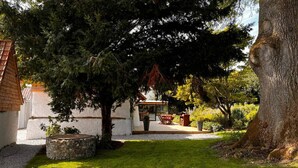 A garden with a stone bench, a small tree, and a building with a tiled roof. - Chambre D'hôtes - Jack Nicklaus (AIX EN ISSART)