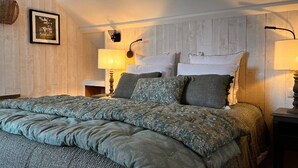 A bedroom with a large bed, two bedside lamps, a framed photo on the wall, and a wooden headboard. - Chambre D'hôtes - Jack Nicklaus (AIX EN ISSART)