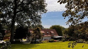 A house with a red-tiled roof, surrounded by a well-maintained lawn and trees. - Chambre D'hôtes - Jack Nicklaus (AIX EN ISSART)