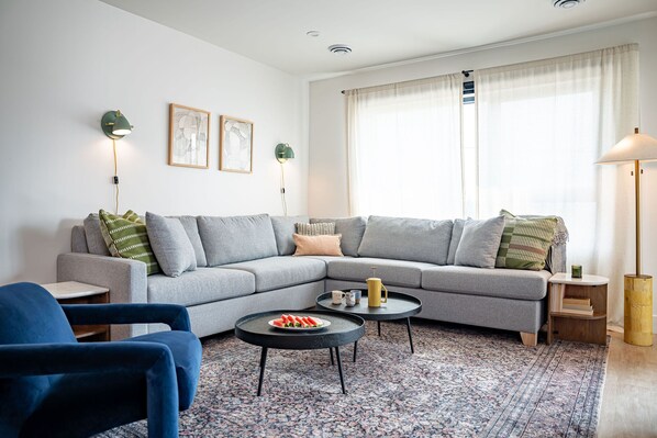 A modern living room with a grey sectional sofa, two black coffee tables, a blue armchair, and a patterned rug. - Cabot Views by Revelstoke Vacations (Revelstoke)