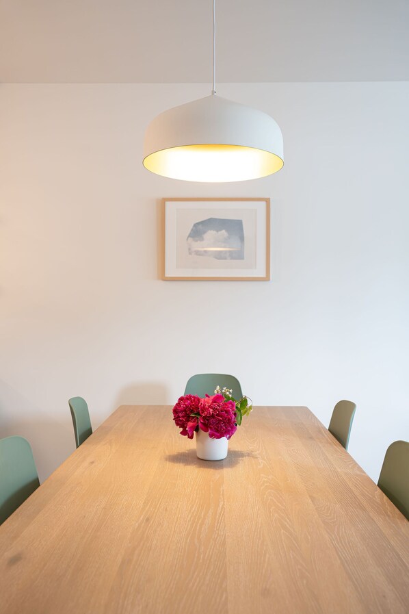 A dining table with a white vase of flowers, a hanging light fixture, and a framed picture on the wall. - Cabot Views by Revelstoke Vacations (Revelstoke)