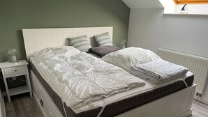 A bed with white bedding, a headboard, and a nightstand with a lamp. - Cozy vacation apartment with dike view in Wremen (Wurster Nordseeküste)