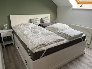 Ein Bett mit weißer Bettwäsche, einem Kopfteil und einem Nachttisch mit Lampe.