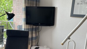 A modern living room with a flat-screen TV mounted on the wall, a comfortable chair, a small white table with a remote control, and a staircase with a handrail. - Cozy vacation apartment with dike view in Wremen (Wurster Nordseeküste)