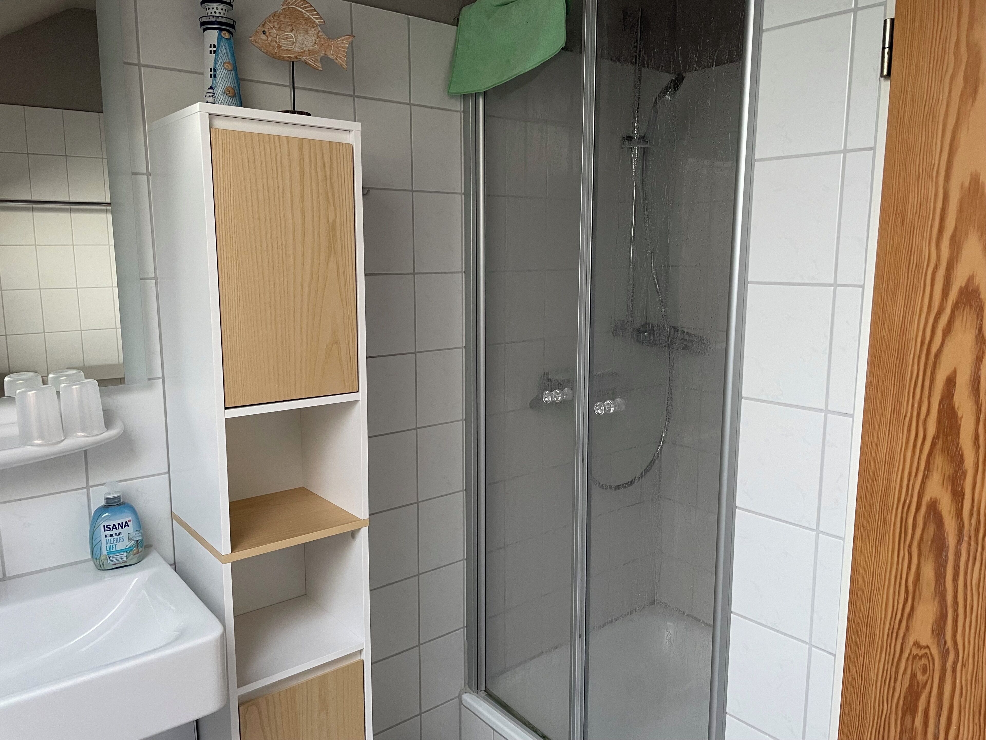 Ein Badezimmer mit einem weißen Waschbecken, einer Holzausstattung, einer Duschkabine aus Glas und einem grünen Handtuch an der Wand.