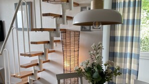 A wooden dining table with a vase of flowers, a modern staircase with white railings, and a window with curtains. - Cozy vacation apartment with dike view in Wremen (Wurster Nordseeküste)