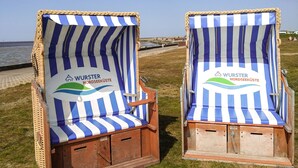 Two beach chairs with striped blue and white fabric and wooden frames, placed on grass near a body of water. - Cozy vacation apartment with dike view in Wremen (Wurster Nordseeküste)