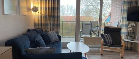A living room with a sofa, a small table, a chair, a TV, and a balcony with a view.