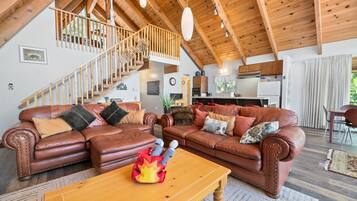 A spacious living room with a wooden staircase, leather sofas, and a dining area.