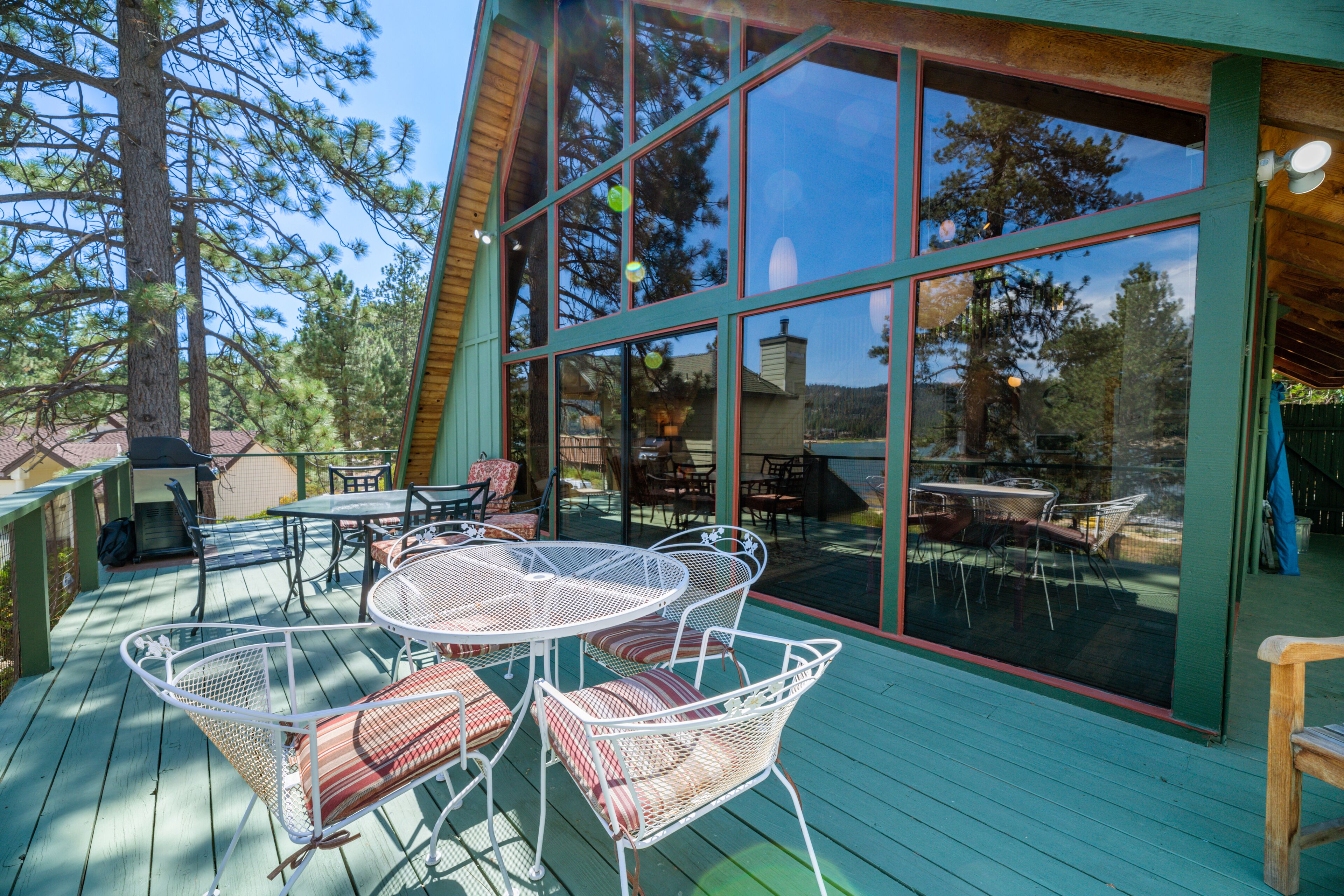A wooden deck with outdoor furniture, large windows, and a view of trees.