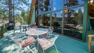 A wooden deck with outdoor furniture, large windows, and a view of trees.