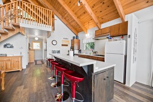 Una cocina amplia con vigas de madera, una isla central con taburetes rojos y un refrigerador blanco.