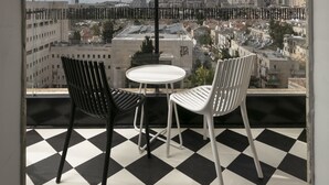 Een balkon met een zwart-wit geruit vloertje, twee stoelen en een tafel.