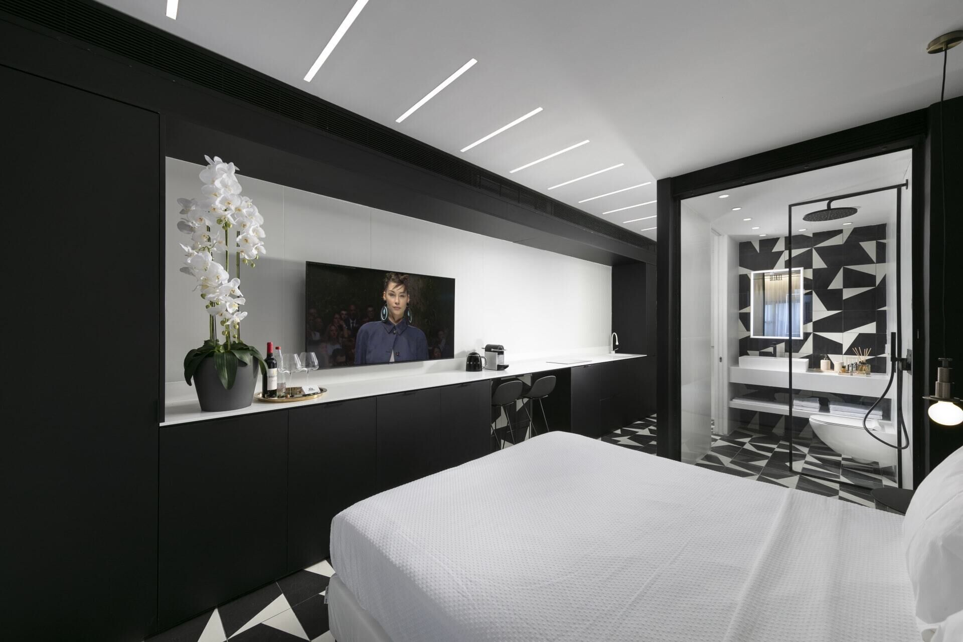 A modern bedroom with a large bed, a TV mounted on the wall, and a bathroom with a geometric tile design.