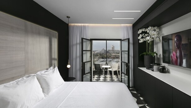 Une chambre d’hôtel moderne avec un grand lit, un balcon doté d’un sol à carreaux et une vue sur la ville.