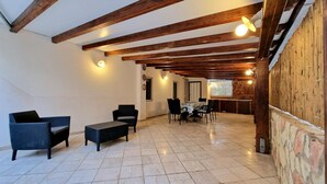 Un soggiorno open space con cucina sullo sfondo, caratterizzato da travi a vista, pavimento piastrellato e un'area pranzo.