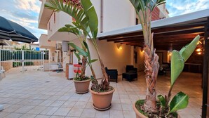 Un'ampia terrazza esterna con piante in vaso, una zona relax coperta e un pavimento piastrellato.